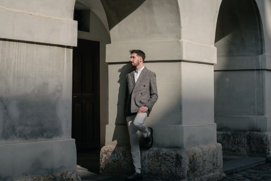 A fashionable man poses against arched architecture, capturing urban elegance.