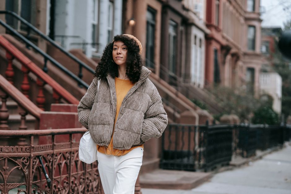 A fashionable woman in a jacket walks confidently on a city sidewalk, showcasing street st