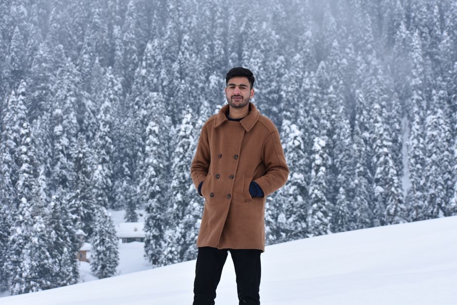 A man in a stylish coat stands in a snowy pine forest. Winter fashion in nature.