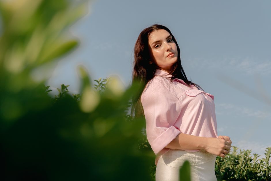 A serene portrait of a woman in a pink blouse standing amidst greenery, basking in natural