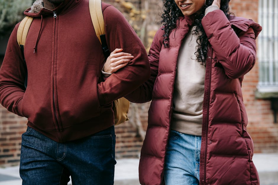 Crop anonymous smiling ethnic woman in outerwear holding black boyfriend with hands in pockets by arm while strolling in town