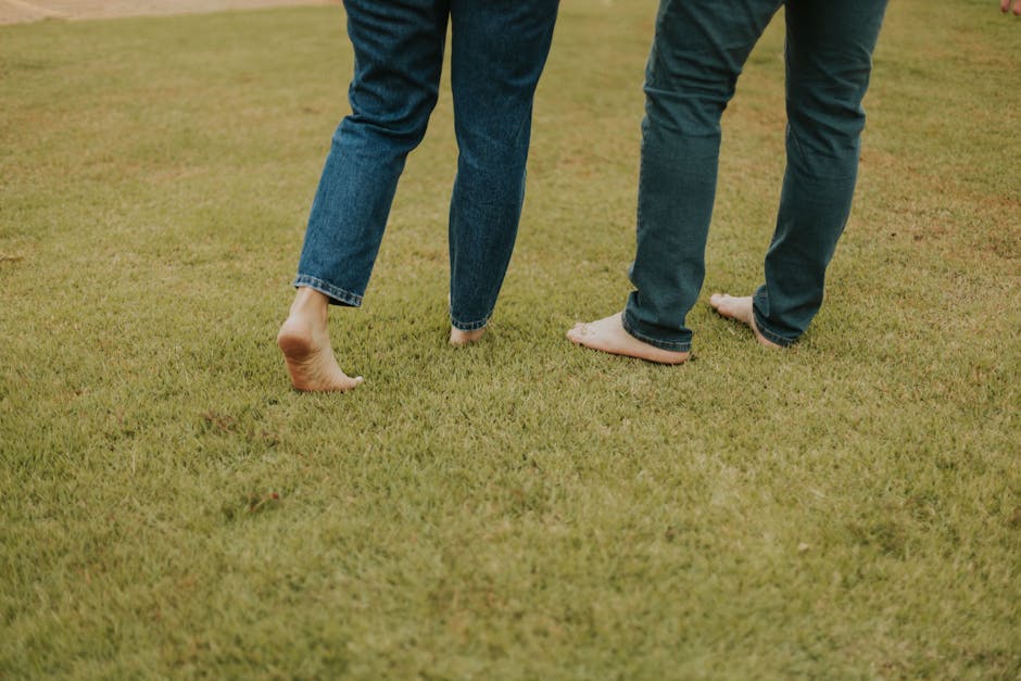 Two people walking barefoot on a grassy field wearing jeans, enjoying nature.