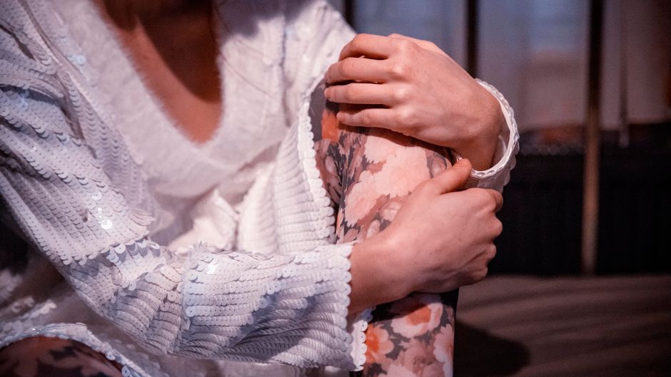 Close-up of a person in a sequined sweater holding their knee adorned with floral-patterne