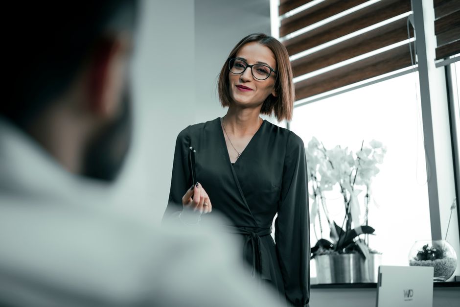 Confident businesswoman in office, holding pen and smiling warmly.