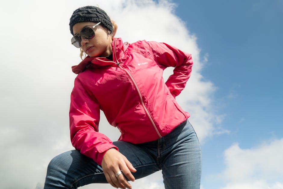 Confident woman in pink jacket posing under a bright blue sky.