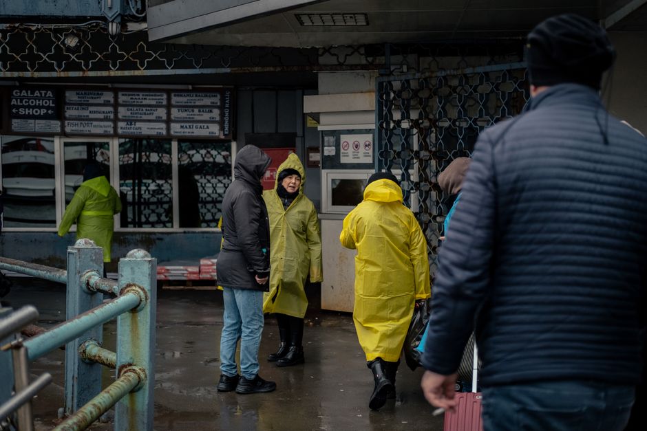 Group of people wearing raincoats walking outside a street market shop on a rainy day.