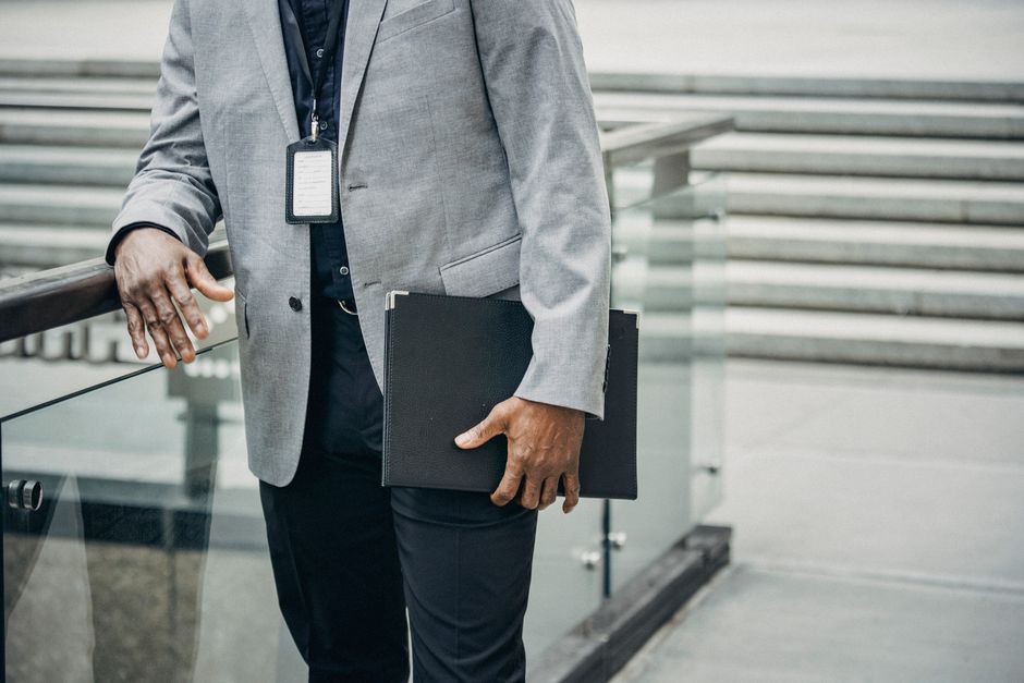 Crop unrecognizable African American entrepreneur leaning on fence and carrying folder with papers in soft daylight