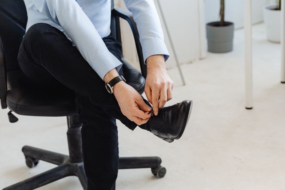 Person in smart casual attire, indoors, tying shoelaces, creating a business-ready look.