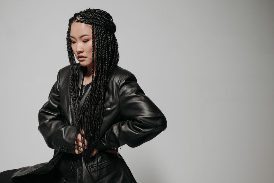 Fashionable woman with braided hair in a black leather jacket poses against a neutral background.
