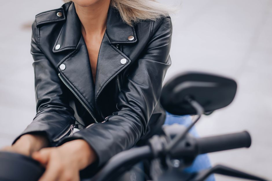 Close-up of a stylish woman wearing a black leather jacket while riding a motorcycle, showcasing modern fashion.
