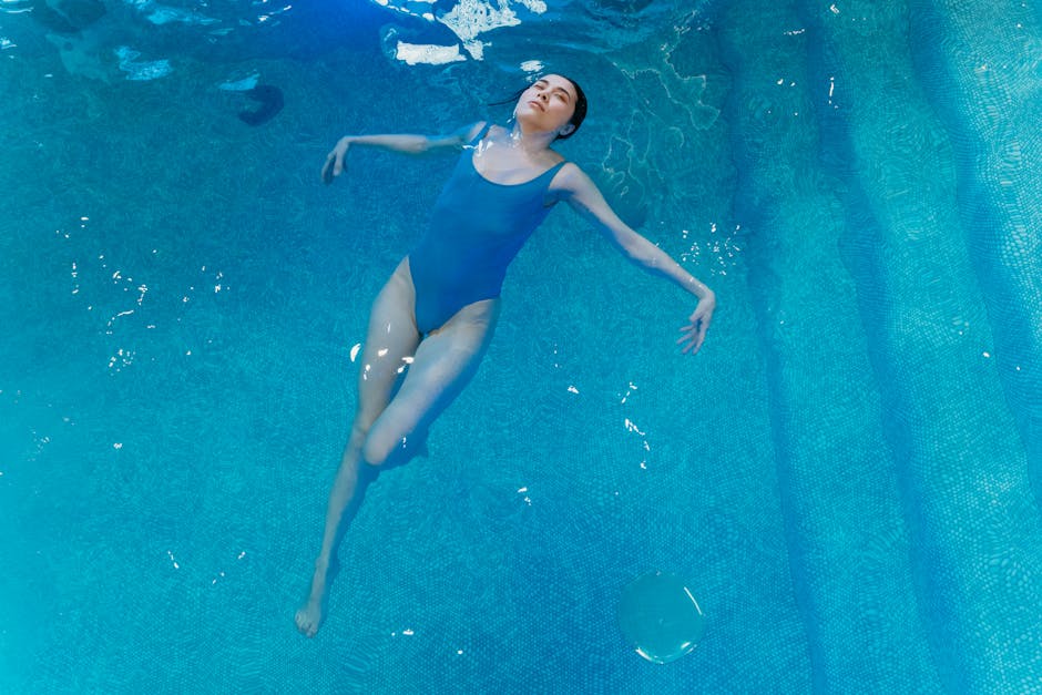 A woman in a blue swimsuit floats peacefully in a swimming pool.