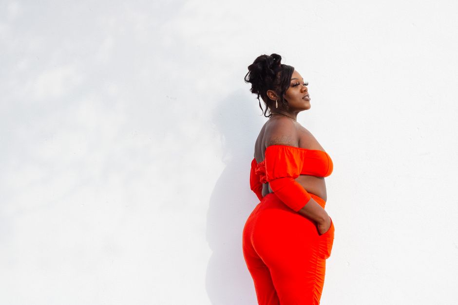 Confident woman posing in a striking orange outfit against a white background.