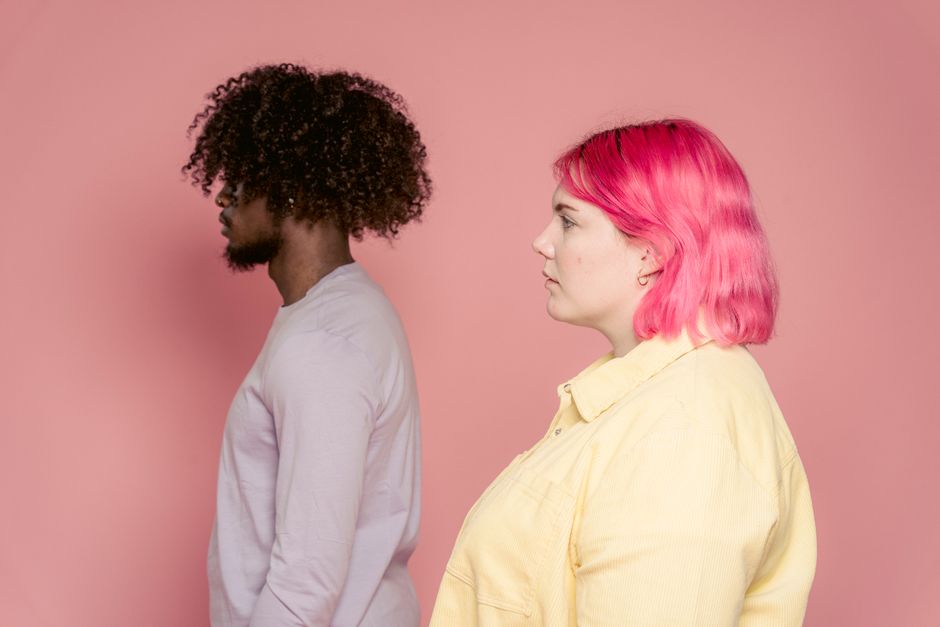 Side view of young plump woman with pink hair against black male partner with Afro hairstyle