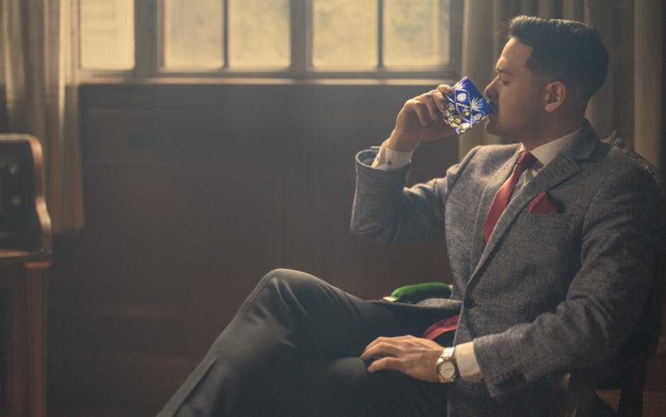 A sophisticated man in formal attire savoring whiskey in a warmly lit classic room.