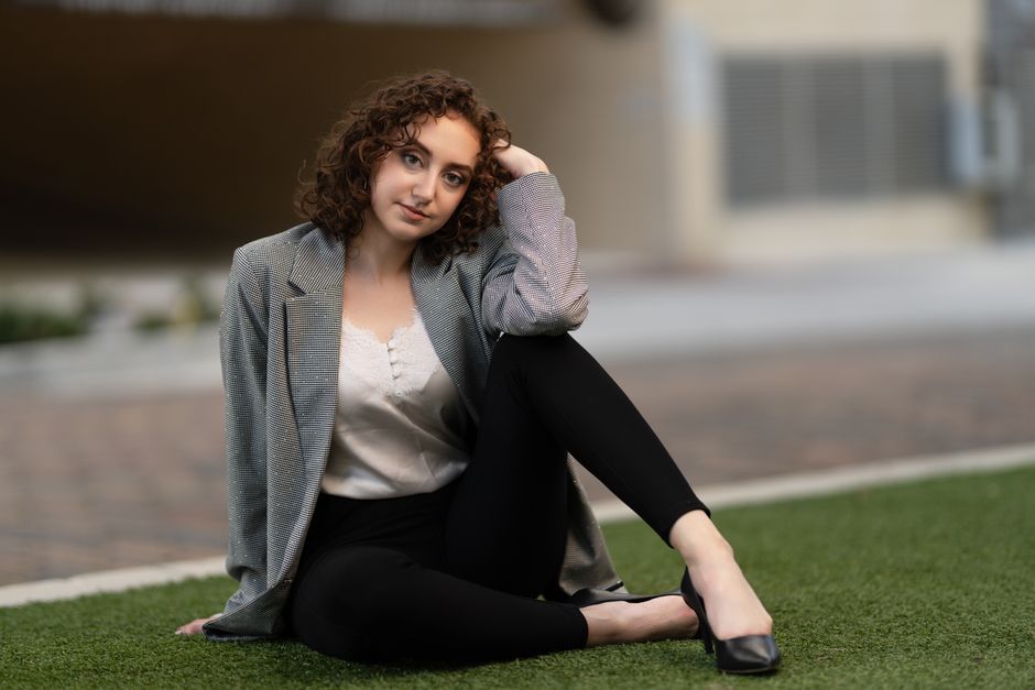 Casual portrait of a young woman sitting on grass in a relaxed pose outdoors.