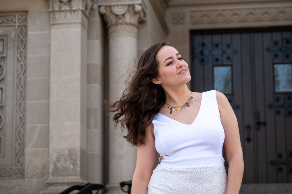 Young woman in a white dress standing by a church entrance, exuding grace and confidence.