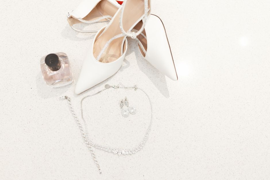 A stylish display of white heels, jewelry, and perfume for wedding day elegance.