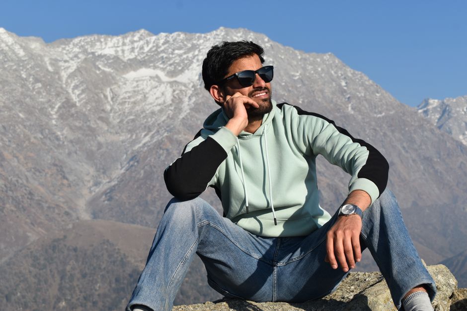 A man sitting in front of scenic mountain background enjoying a sunny day.