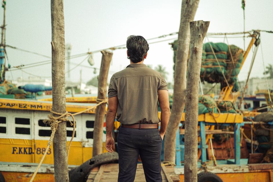A man stands on a dock overlooking fishing boats at a harbor, conveying solitude.