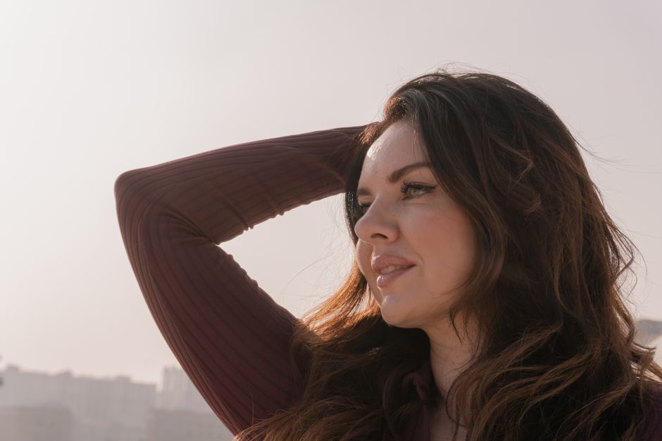 A thoughtful woman poses outdoors with a city skyline in soft focus.
