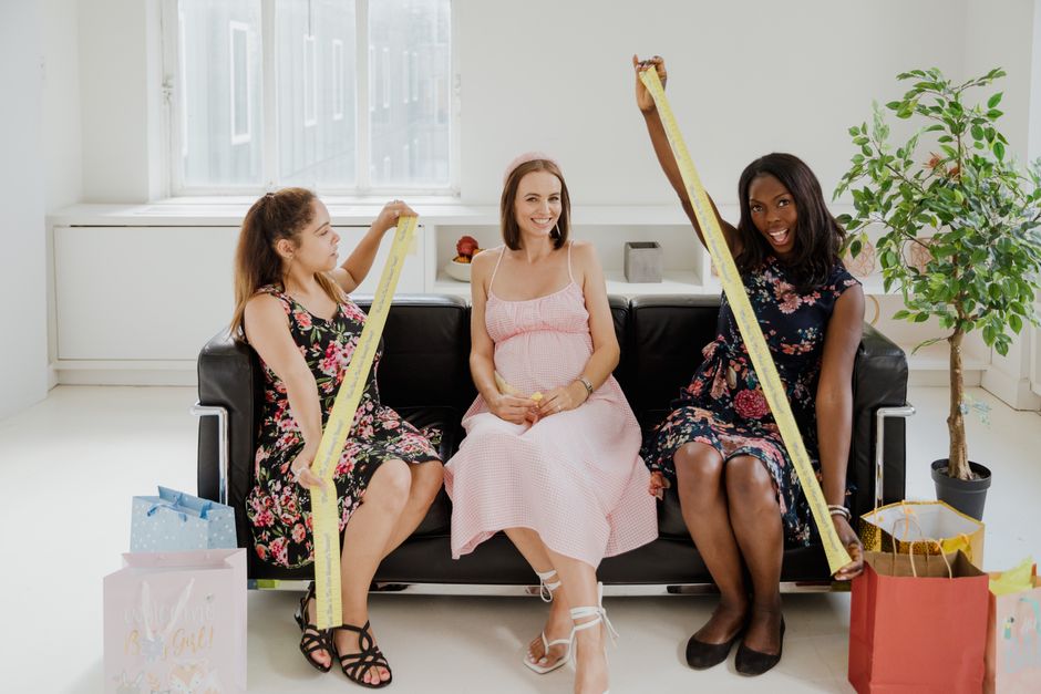 Pregnant woman surrounded by friends at a joyful baby shower celebration indoors.