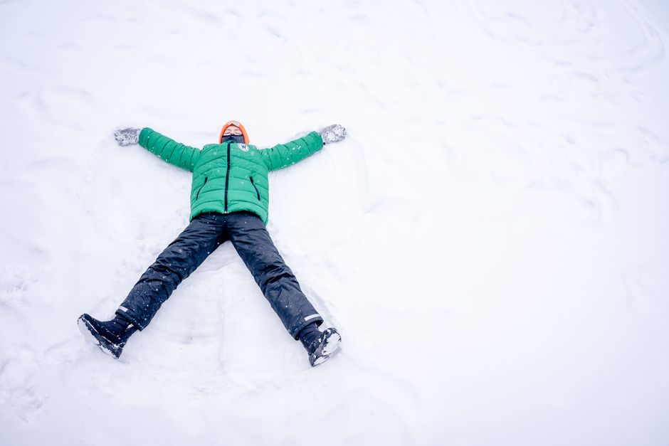 Child lying in the snow with outstretched arms, dressed in winter clothing and enjoying a frosty day.