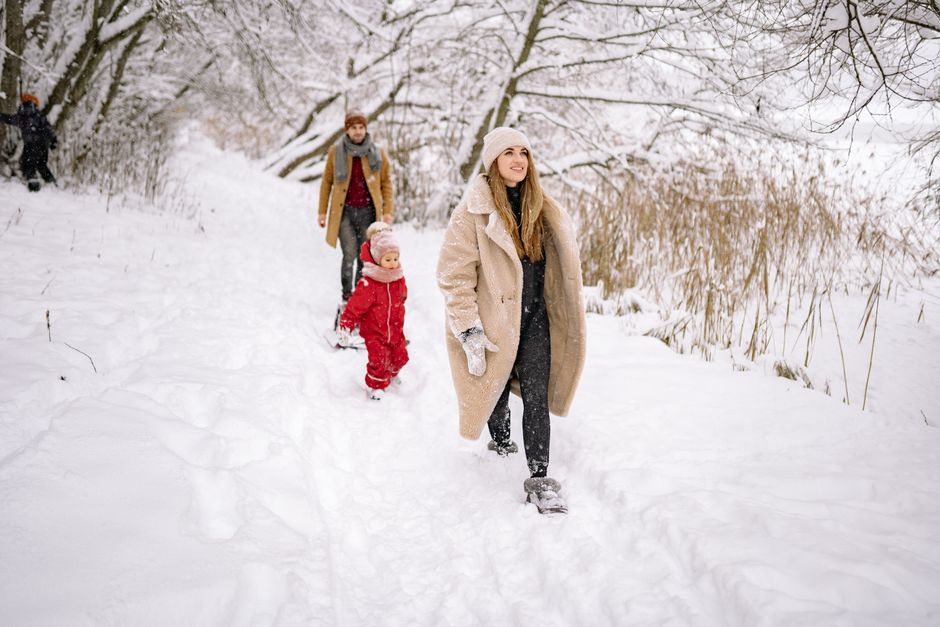 A joyful family walking through a snowy, scenic park in winter clothing.