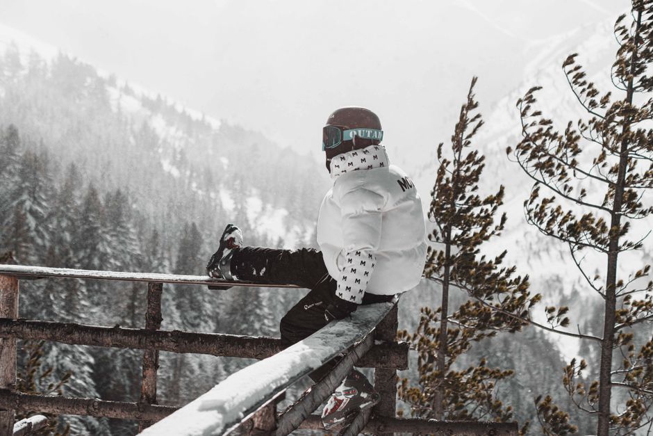 A person in winter gear sits on a railing, overlooking a snowy forest landscape in Brezovica, Serbia.